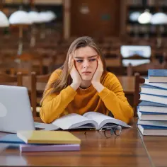 Zmęczona studentka pochyla się nad książkami w bibliotece, próbując zrozumieć trudną historię 2.