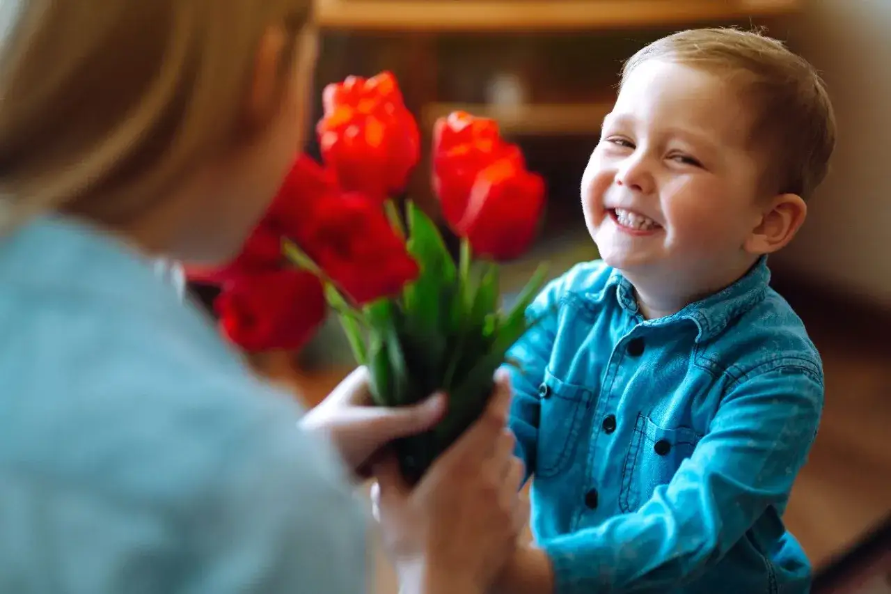 Uśmiechnięty chłopiec wręcza mamie bukiet czerwonych tulipanów. To piękny krótki wierszyk dla rodziców, pełen miłości.