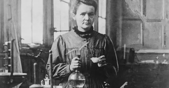Maria Skłodowska-Curie w laboratorium, trzymająca kolbę i próbówkę. Ciekawostki o jej pracy z polonem i radem.